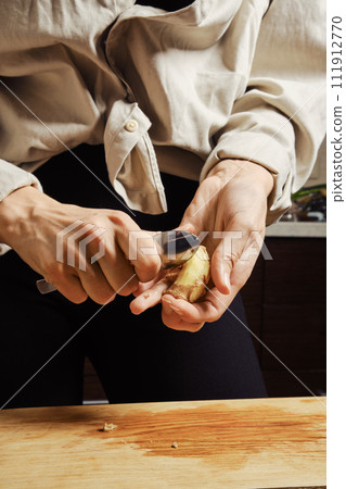 Unrecognizable woman peeling ginger with spoon 111912770