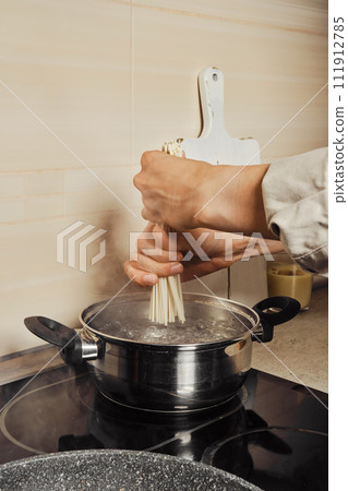 Unrecognizable woman putting noodles into boiling water Unrecognizable woman putting noodles into boiling water 111912785