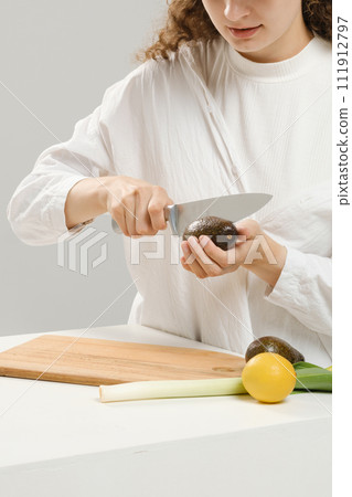 Unrecognizable woman cutting fresh avocado into halves 111912797