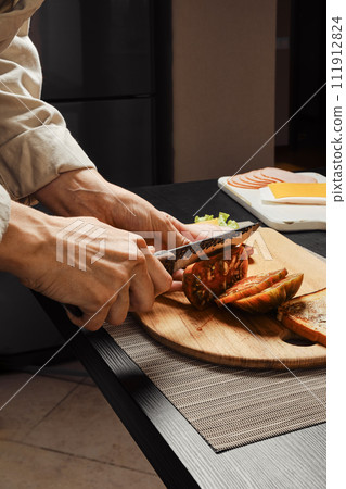 Side view of hands of unrecognizable woman cutting tomato for sandwich 111912824