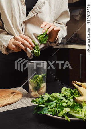 Unrecognizable woman drops spinach into blender 111912826