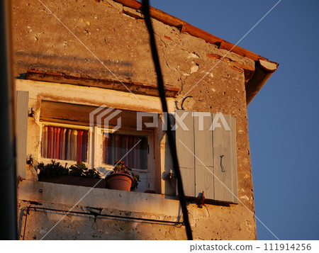 Antique stone house in the old town. Window under roof. Colored thread curtains Antique stone house in the old town. Window under roof. Colored thread curtains 111914256