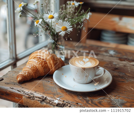 Cozy cafe setting featuring a cup of cappuccino with latte art beside a freshly baked croissant Cozy cafe setting featuring a cup of cappuccino with latte art beside a freshly baked croissant 111915702