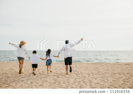 A heartening family scene on the beach parents holding hands running and jumping with their children in holiday laughter. Illustrating the happiness and togetherness of a carefree beach vacation. 111916356