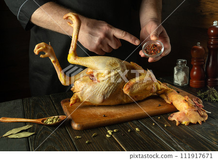 Chef preparing raw rooster in saloon kitchen. Before roasting, the cook adds spices to the rooster. Preparing to make an old-fashioned fried chicken recipe Chef preparing raw rooster in saloon kitchen. Before roasting, the cook adds spices to the rooster. Preparing to make an old-fashioned fried chicken recipe 111917671