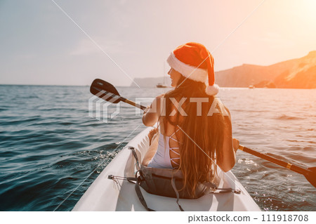 Woman in kayak back view. Happy young woman in Santa hat floating in kayak on calm sea. Summer holiday vacation and cheerful female people relaxing having fun on the boat. Woman in kayak back view. Happy young woman in Santa hat floating in kayak on calm sea. Summer holiday vacation and cheerful female people relaxing having fun on the boat. 111918708