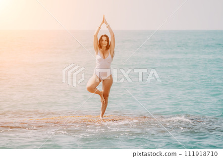 Woman sea yoga. Back view of free calm happy satisfied woman with long hair standing on top rock with yoga position against of sky by the sea. Healthy lifestyle outdoors in nature, fitness concept Woman sea yoga. Back view of free calm happy satisfied woman with long hair standing on top rock with yoga position against of sky by the sea. Healthy lifestyle outdoors in nature, fitness concept 111918710