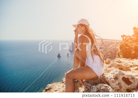 Woman summer travel sea. Happy tourist enjoy taking picture outdoors for memories. Woman traveler posing over sea bay surrounded by volcanic mountains, sharing travel adventure journey 111918713