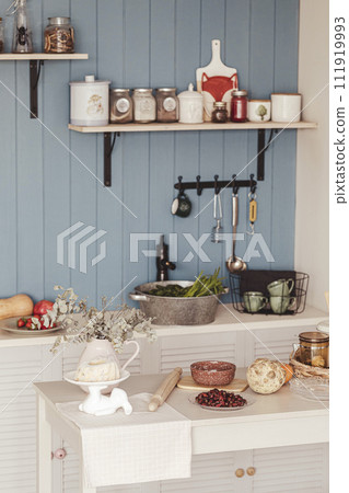 Piece of interior and tableware, some greenery and berries on a white table in the kitchen at a country cottage, indoor, vertical photo, selective focus. Piece of interior and tableware, some greenery and berries on a white table in the kitchen at a country cottage, indoor, vertical photo, selective focus. 111919993