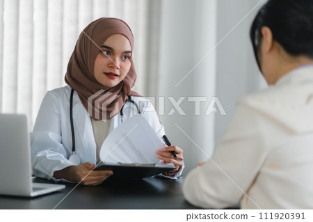 Young muslim female doctor in brown hijab headscarf having appointment consulting female patient in modern clinic hospital. Medical healthcare concept. 111920391