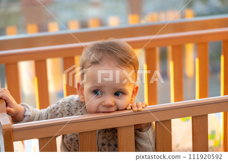 baby sadly bites the edge of the crib with his teeth while waiting for his parents 111920592