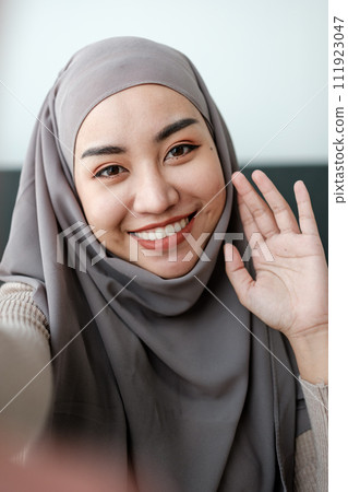 A Beautiful asian woman in hijab talks on video call, online meeting with colleagues and clients, woman cheerfully waves her hand and greets interlocutors online. A Beautiful asian woman in hijab talks on video call, online meeting with colleagues and clients, woman cheerfully waves her hand and greets interlocutors online. 111923047
