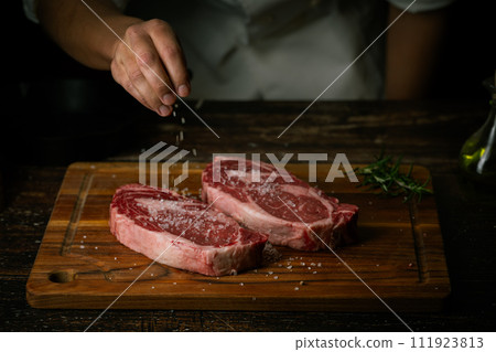 chef seasoning steak with salt and pepper 111923813
