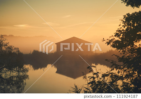 Old barn on lake shore on misty sunrise Old barn on lake shore on misty sunrise 111924187