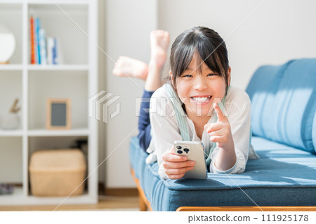 An elementary school girl operates a smartphone in the living room. An elementary school girl operates a smartphone in the living room. 111925178