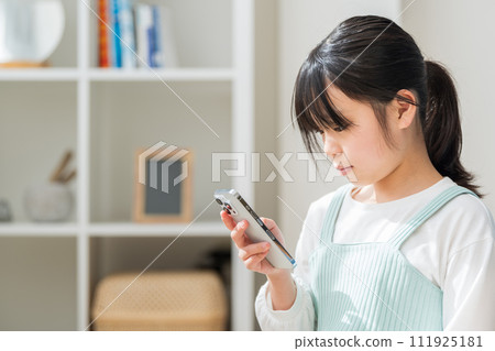 一名小學生在客廳操作智慧型手機。 111925181
