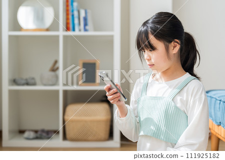 一名小學生在客廳操作智慧型手機。 111925182