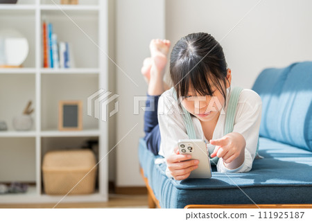 An elementary school girl operates a smartphone in the living room. 111925187