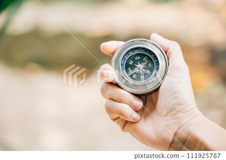 A traveler hand cradles a compass in a park signifying the search for direction and guidance. Amidst nature beauty the compass represents exploration and discovery. 111925787