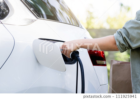 Woman with shopping bag next to a charging electric car. Woman with shopping bag next to a charging electric car. 111925941