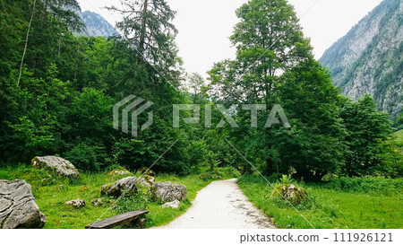 Konigssee, Germany - 06.16.2018: An empty trail to Obersee with grass on the side and Alps in the back on a sunny day 111926121