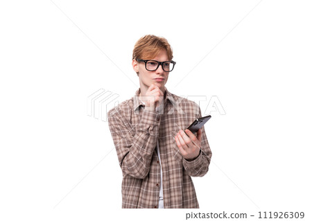 young european man with red hair wearing glasses and a plaid shirt holding a smartphone and thinking 111926309