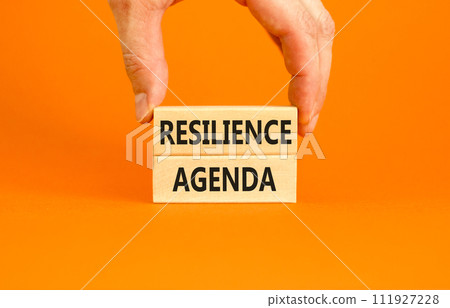 Resilience agenda symbol. Concept word Resilience agenda typed on wooden blocks. Beautiful orange table orange background. Businessman hand. Business and resilience agenda concept. Copy space. 111927228