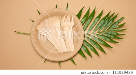 Paper plates, wooden spoons and forks on a beige background 111929489