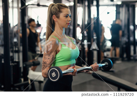 Pretty woman concentrated in her workout and doing biceps curls with ez-bar at the gym 111929720