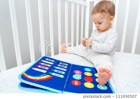 Baby playing with montessori quiet book sitting in a crib. Concept of smart books and modern educational toys 111930507