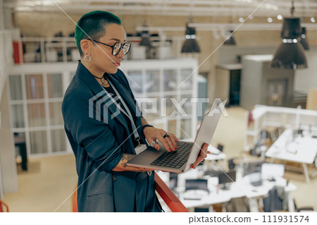 Focused tattooed female business owner is use laptop standing on modern coworking background 111931574