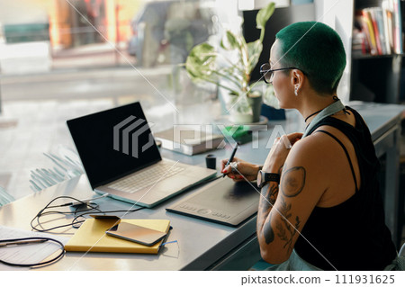Woman designer uses graphics tablet and laptop for retouching photos or digital drawing in workshop 111931625