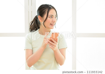 A young woman looking at her smartphone by the window A young woman looking at her smartphone by the window 111933142