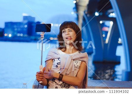 A girl takes pictures of herself on her phone at night in the city 111934102