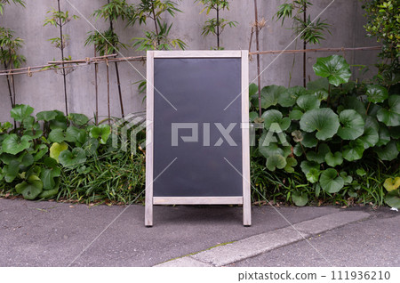 Blank white outdoor advertising stand/sandwich board mock up template. Clear street signage board placed by an outdoor dinning area of a restaurant. Background texture of standee on street. Blank white outdoor advertising stand/sandwich board mock up template. Clear street signage board placed by an outdoor dinning area of a restaurant. Background texture of standee on street. 111936210