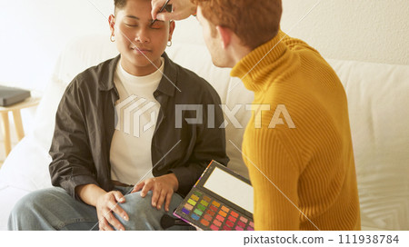 Gay man applying eye shadow to a man Gay man applying eye shadow to a man 111938784