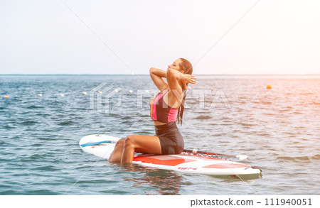 Sea woman sup. Silhouette of happy young woman in pink bikini, surfing on SUP board, confident paddling through water surface. Idyllic sunset. Active lifestyle at sea or river Sea woman sup. Silhouette of happy young woman in pink bikini, surfing on SUP board, confident paddling through water surface. Idyllic sunset. Active lifestyle at sea or river 111940051
