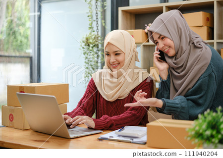 Friend muslim female two work business sme online shopping working on laptop computer with parcel box on desk at home, SME online business and delivery concept 111940204