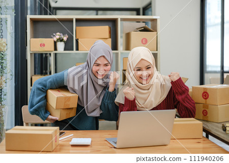 Friend muslim female two work business sme online shopping working on laptop computer with parcel box on desk at home, SME online business and delivery concept 111940206