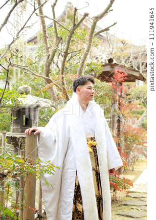 銀色和白色的男士褲裙搭配時尚的長外罩,成年男子穿著鳳紋褲裙,成年儀式外景拍攝 銀色和白色的男士褲裙搭配時尚的長外罩,成年男子穿著鳳紋褲裙,成年儀式外景拍攝 111941645