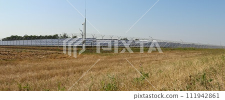 a dry field with solar panels surrounded by a fence on a sunny day as an example of the work of environmentally friendly technologies, a country landscape with batteries of a modern power plant a dry field with solar panels surrounded by a fence on a sunny day as an example of the work of environmentally friendly technologies, a country landscape with batteries of a modern power plant 111942861