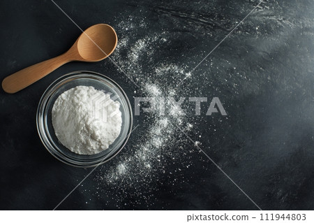 Top view of hydrolyzed collagen powder in a glass bowl with wooden spoon on a black background 111944803