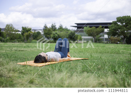 A woman wearing yoga wear lying on her back in a park A woman wearing yoga wear lying on her back in a park 111944811