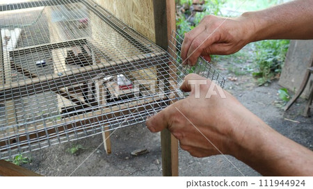 male hands bend the mesh side of the metal lattice base of a cage for domestic quails in the production process, forming a rise in the edge of the cage base for small farm poultry 111944924