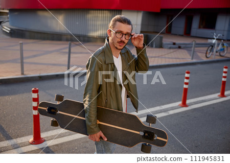 Portrait of handsome casual guy with skateboard over downtown background 111945831