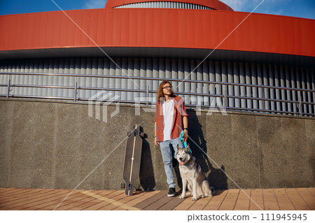Hipster man riding skateboard with dog on leash enjoying summer time 111945945