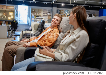 Man and woman loving couple sitting in armchairs while choosing one for home Man and woman loving couple sitting in armchairs while choosing one for home 111945965