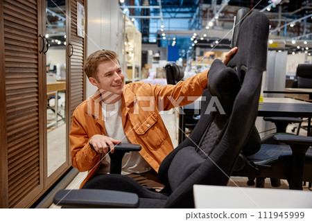 Young handsome man making decision what home office armchair to buy Young handsome man making decision what home office armchair to buy 111945999