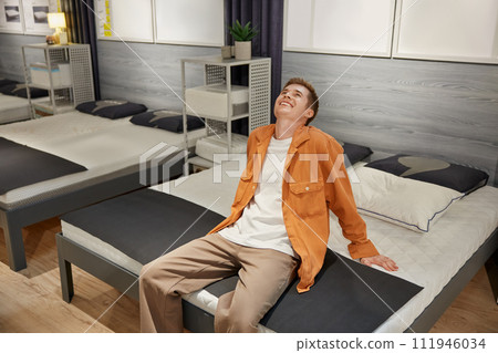 Handsome male customer sitting on new bed at furniture store 111946034