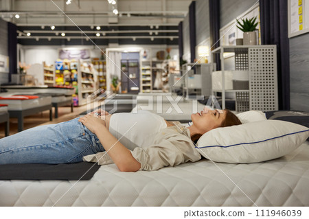 Young woman shopper choosing new bed at modern furniture showroom Young woman shopper choosing new bed at modern furniture showroom 111946039